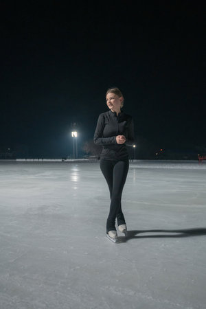 Beautiful young woman ice skating and performing short program over city outdoor ice arena. Winter activities conceptの写真素材