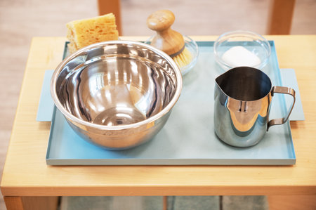 A collection of kitchen prep tools, including a stainless steel bowl, pitcher, brush, and sponge,...