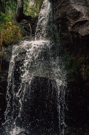 Close-up of a small waterfall flowing over a rocky cliff surrounded by lush greenery, serene natural landscape.の写真素材