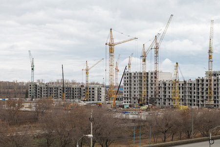 A large urban construction site with multiple tower cranes erecting modern apartment buildings under a cloudy sky.の写真素材
