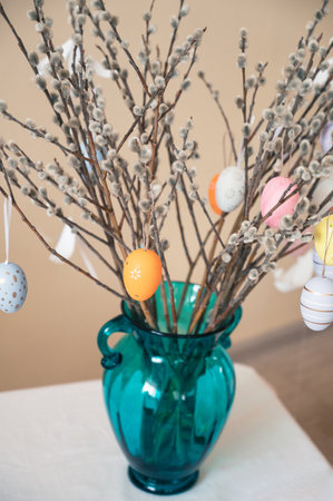 Decorative Easter eggs in various pastel colors hang on pussy willow branches arranged in a vase, creating a festive Easter centerpiece.の写真素材