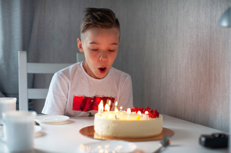 Smiling young boy leaning on a table with a lit birthday cake, enjoying a joyful celebration in a cozy setting.の写真素材