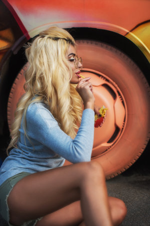 A fashionable young woman with blonde hair and glasses enjoys a snack while sittingの写真素材