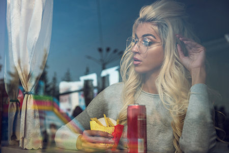 A fashionable young woman with blonde hair and glasses enjoys a snack