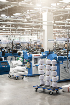 View of automated textile manufacturing machines in a factory, with spools of white thread ready for...