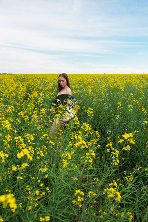 A young woman stands in a vast yellow flower field, holding a round mirror. She gazes calmly, blending with the serene natural scenery.の写真素材