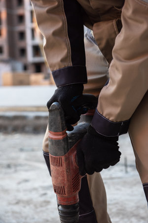 Close-up of a construction worker operating a power drill on a building site, wearing safety gear and work boots.の写真素材