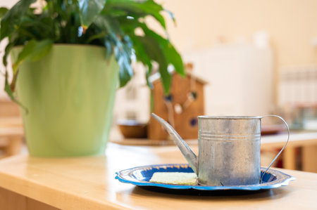 Close-up of a rustic metal watering can on a blue tray beside a green potted plant, creating a cozy indoor scene.の写真素材