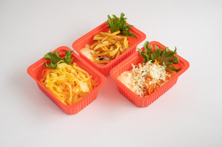 Three red plastic containers holding an assortment of salads and fries with garnishes, for takeaway or ready-to-eat meals.の写真素材