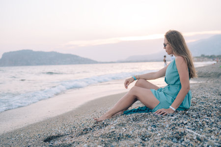 A woman in a flowing green dress poses on the beach at sunset.の写真素材