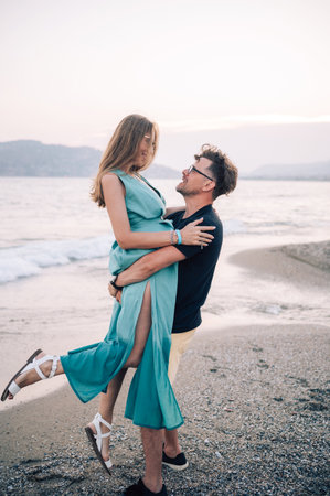 A smiling couple shares a joyful moment on the beach at sunset, with the man lifting the woman playfully near the sea waves, Alanya, Turkeyの写真素材