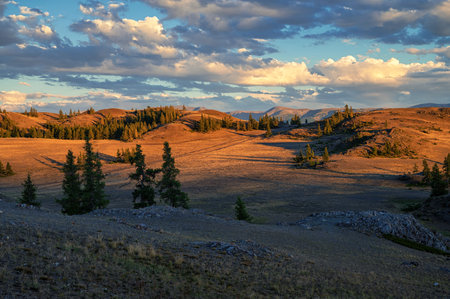 A breathtaking sunset over a rugged mountain landscape, casting warm golden light across hills, trees, and rocky terrain.の写真素材