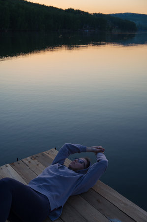 Woman lying down on the pier at lake, closeup portrait, summer sunsetの写真素材