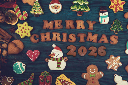 Colorful Christmas cookies shaped like snowmen, trees, stars, and gingerbread surround the text Merry Christmas 2026 on a wooden background.の写真素材