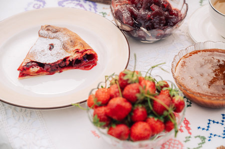 Homemade cherry pie slice with powdered sugar served with fresh strawberries, fruit preserves and tea on a cozy table setting.の写真素材