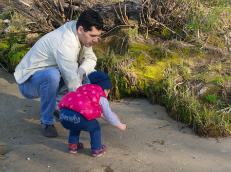 Young father and his adorable little daughter drawing on the sand  at beach