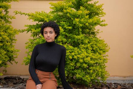 Beautiful woman with curly hair sitting with green tree in backgroundの写真素材