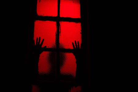Silhouette of person touching window in darkの写真素材