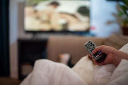 Close up shot of hand holding remote and pointing it at the television