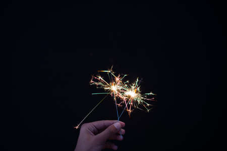 Close up shot of hand holding sparklers against dark background