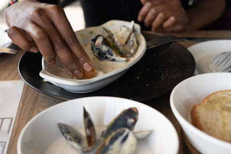 Woman eating mussels out of plate at restaurantの写真素材