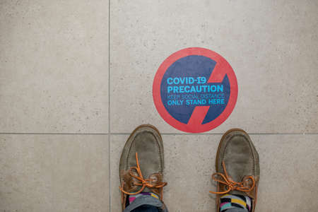 Feet standing next to social distance sign on floorの写真素材