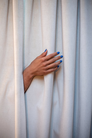 Hand sticking out of curtain with blue nail polishの写真素材