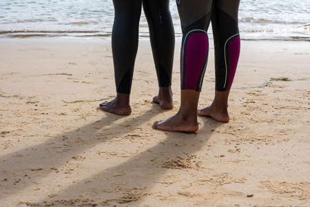 Cropped shot of two woman in wetsuits standing at shoreの写真素材