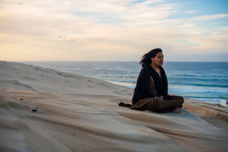 Woman sitting on sand dune at the beachの写真素材