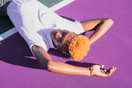 Young man with colorful hair laying on tennis courtの写真素材