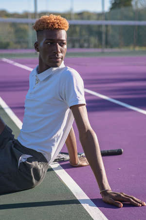 Portrait of young man sitting on tennis courtの写真素材