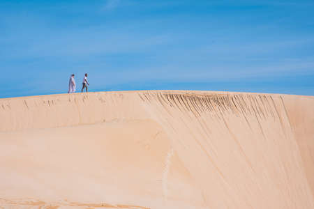 Landscape shot of couple seen walking along duneの写真素材