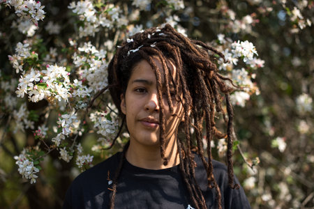 Portrait of woman with locs standing against blooming tree