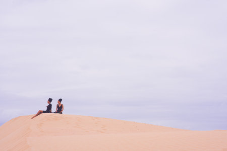 Two woman seen sitting on edge of sand duneの写真素材
