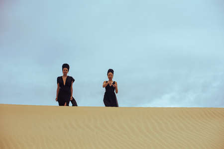 Two woman seen walking on top of sand duneの写真素材