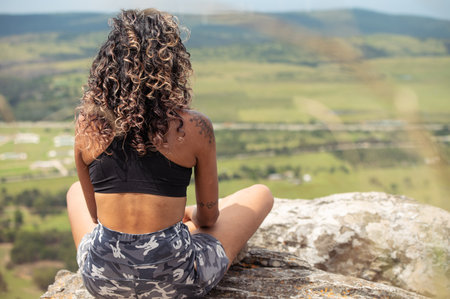 Rear view of woman sitting on rock and looking aheadの写真素材