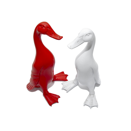 Red and white goose sculptures stand on a white tableの写真素材