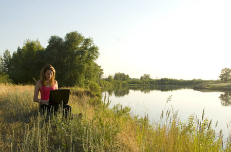 young pretty woman with notebook on the river bankの写真素材