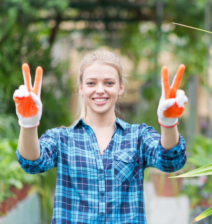 young beautiful female gardener with v sign in greenhouseの写真素材
