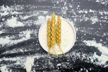 wheat flour and ears in a bowl on black backgroundの写真素材