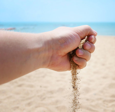 Hand with sand against tropical seaの写真素材