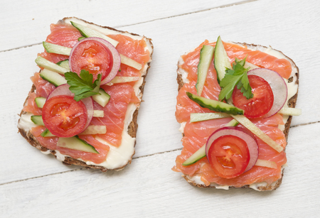 Two open sandwiches with red fish, tomato, radish and cucumber on wooden backgroundの写真素材