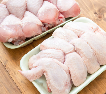 Two trays of chicken wings and legs are displayed on a wooden table. The wings are cut into pieces and are ready to be cookedの写真素材
