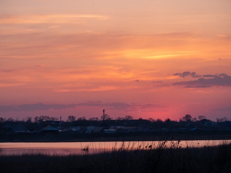 The sky is a beautiful orange color as the sun sets. The clouds are scattered throughout the sky, creating a peaceful and serene atmosphereの写真素材