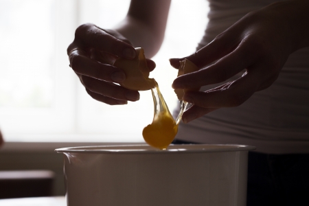 hands opening broken eggshell of brown raw egg