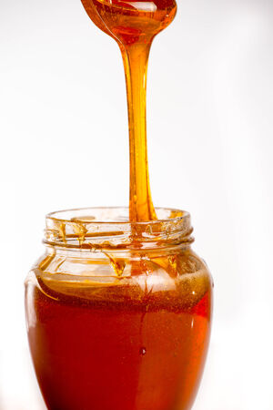 glass of fresh honey on white の写真素材