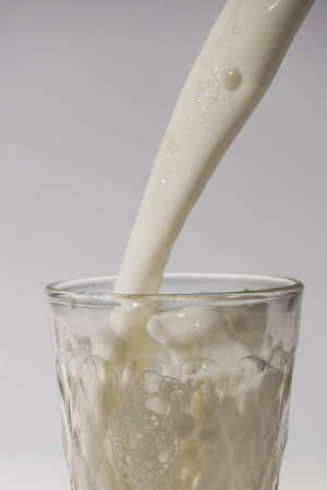 pouring milk in a glass isolated against white の写真素材