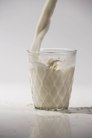 pouring milk in a glass isolated against white の写真素材