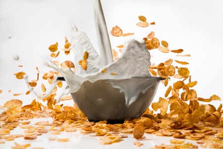 Corn flakes with milk pouring from glass