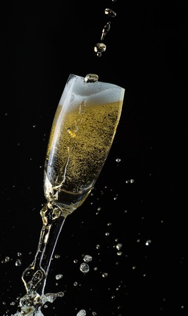 Glass of champagne with splash, isolated on black backgroundの写真素材